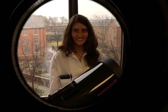 Menina branca com cabelo preto sorri para a foto segurando a lente de um telescópio.(foto: Arquivo Pessoal)