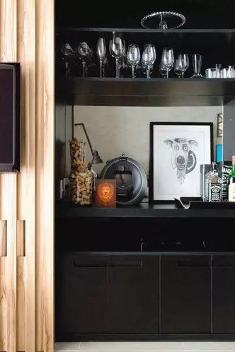 Os proprietários desse bar não gostariam que ele ficasse exposto o tempo todo. Então, as arquitetas da Triarq Studio Arquitetura desenharam um móvel que pudesse ser camuflado por um painel retrátil e ripado. Espelho, vaso com rolhas, quadro, taças variadas e caixa de som agregam personalidade ao nicho.(foto: Carla Daqui/Divulgação) Os proprietários desse bar não gostariam que ele ficasse exposto o tempo todo. Então, as arquitetas da Triarq Studio Arquitetura desenharam um móvel que pudesse ser camuflado por um painel retrátil e ripado. Espelho, vaso com rolhas, quadro, taças variadas e caixa de som agregam personalidade ao nicho.(foto: Carla Daqui/Divulgação)