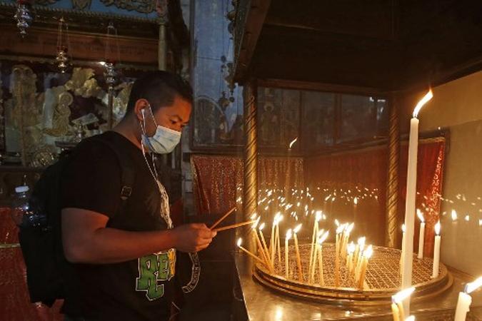 Um adorador cristão acende velas na Igreja da Natividade de Belém, após sua reabertura, quando as autoridades palestinas diminuíram as restrições aos coronavírus na Cisjordânia ocupada.(foto: Musa Al SHAER / AFP) Um adorador cristão acende velas na Igreja da Natividade de Belém, após sua reabertura, quando as autoridades palestinas diminuíram as restrições aos coronavírus na Cisjordânia ocupada.(foto: Musa Al SHAER / AFP)
